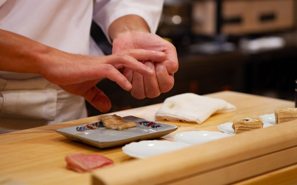 A chef shaping nigiri sushi by hand at a hinoki wood counter